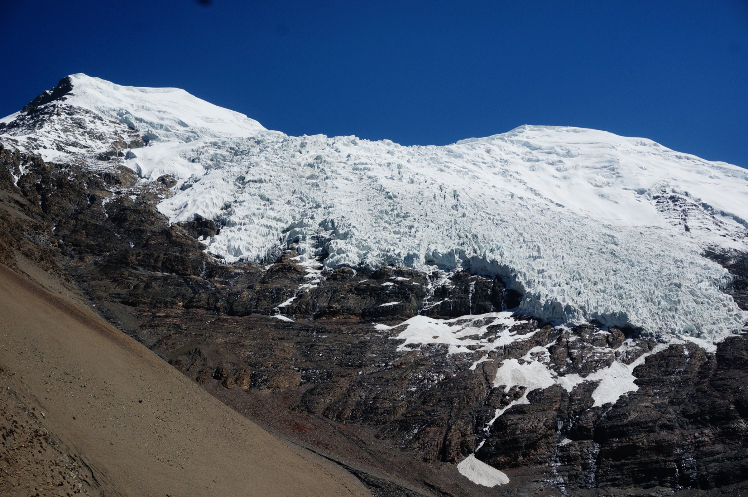 Mountain glacier surrounded by dark rock and snow-covered summits